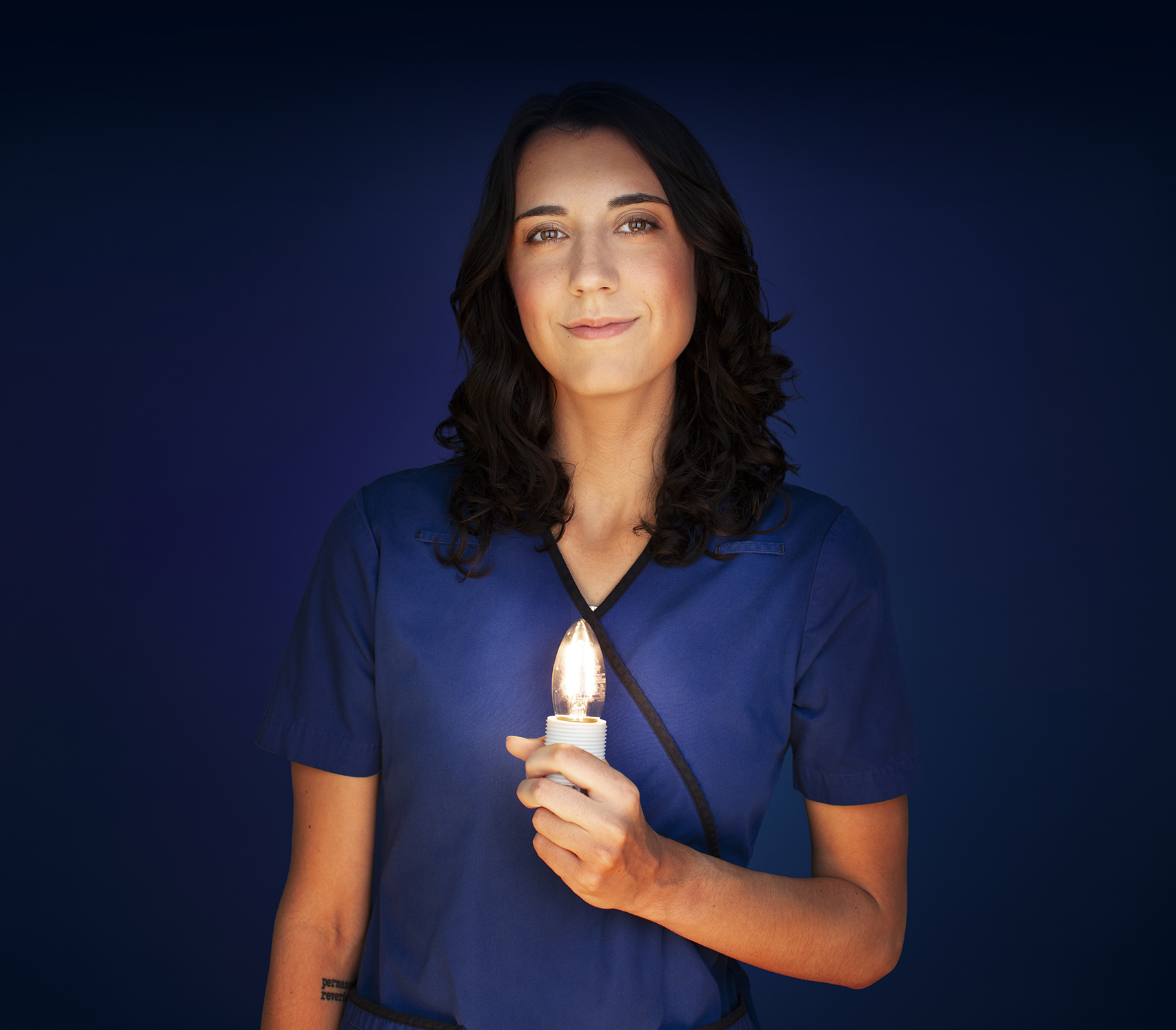 Sainte-Justine nurse Sandrine, wearing blue hospital scrubs and proudly holding a glowing candle-shaped light in her left hand.