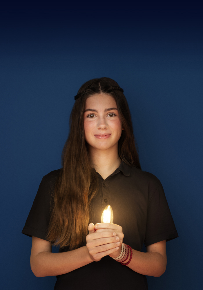 Mia,13 ans, porte un polo noir et une jupe rouge à carreaux, sourit et tient une ampoule allumée dans ses mains.