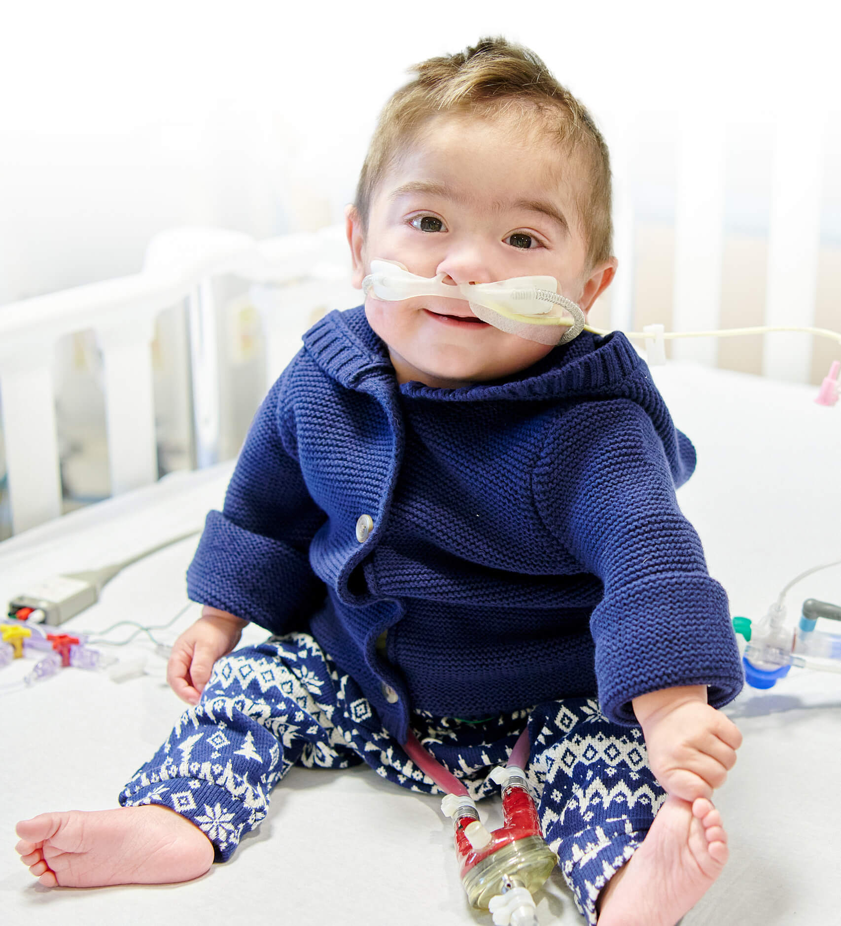 Éliam, un an, est assis dans son lit d’hôpital au CHU Sainte-Justine où il est hospitalisé depuis plus d’un an, en attente d’un nouveau cœur.