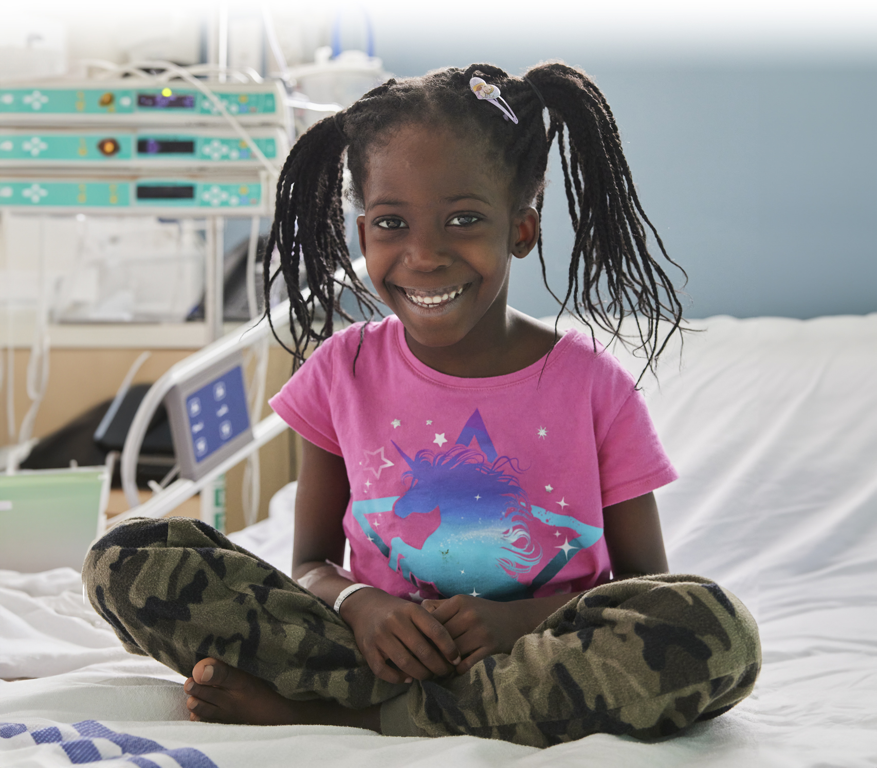 Lily, une patiente du Centre de cancérologie Charles-Bruneau du CHU Sainte-Justine est assise, souriante sur son lit d'hôpital.