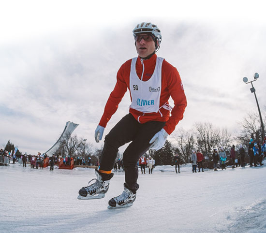 Un patineur casqué, au corps incliné dans un virage, sur une patinoire extérieure.